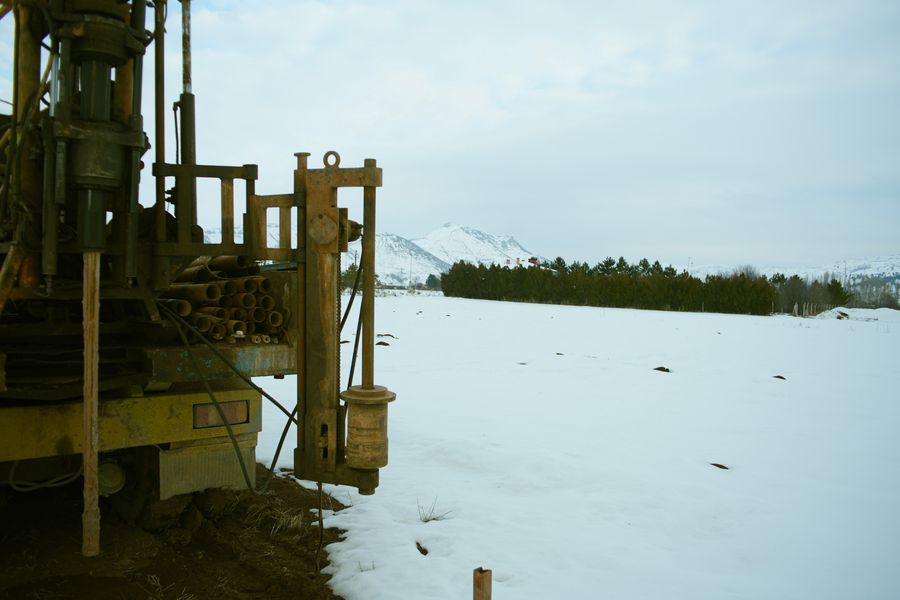 Drilling rig working in a wide snowy field with mountains in the background