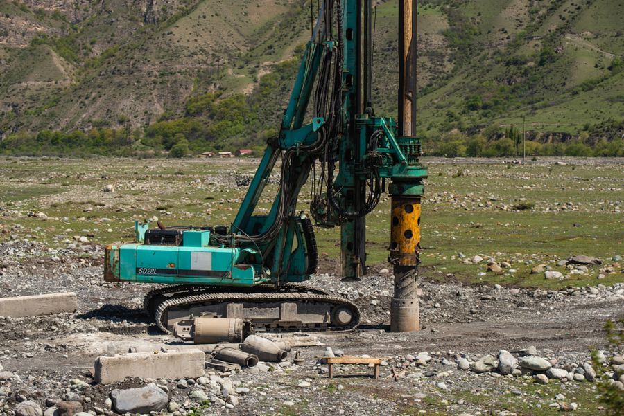 Large teal drilling rig in a rocky valley with green hills